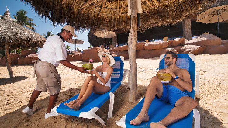 Refréscate con cocteles tropicales en la playa bajo cabañas de palapas con servicio de playa de nuestros bares